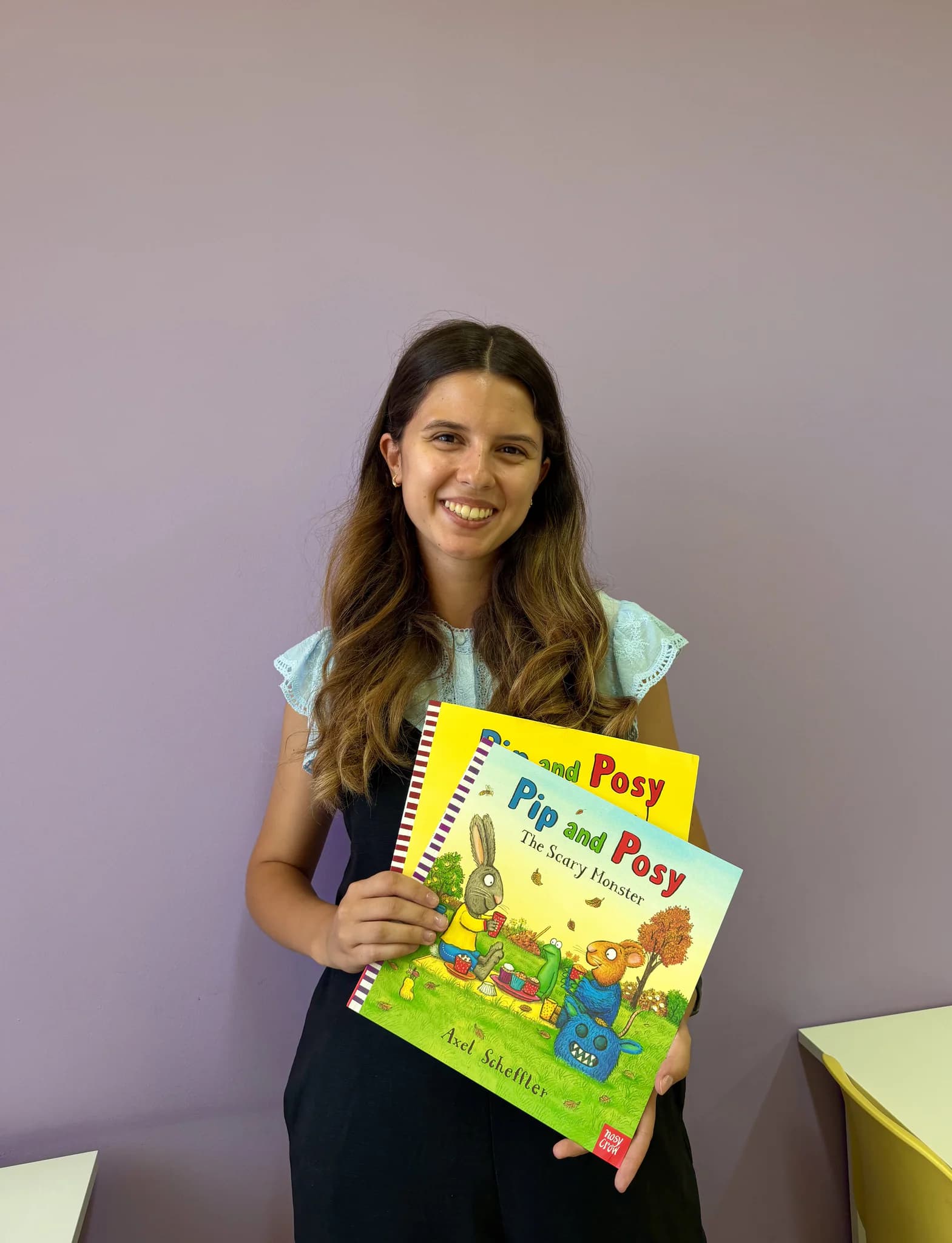 Улыбающаяся учительница держит детские книги Pip and Posy на английском языке